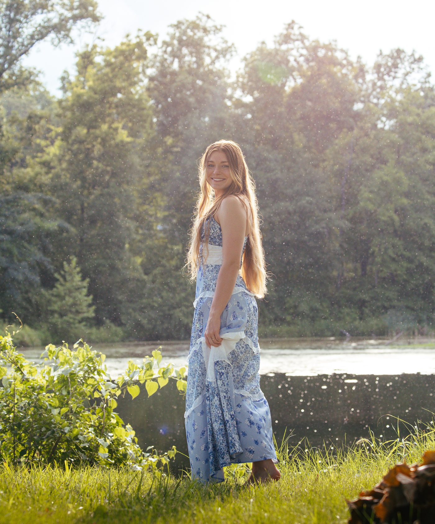 Full-length portrait in a floral dress standing by a pond at golden hour