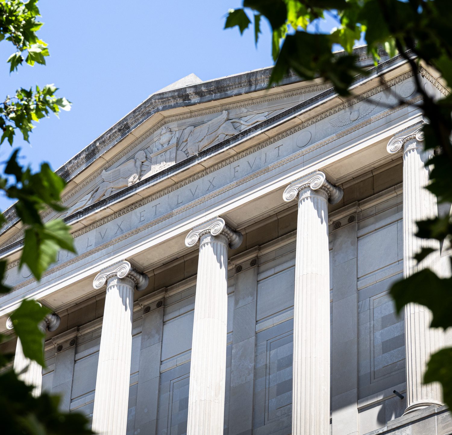 Neoclassical building pediment with Ionic columns and a Latin inscription, framed by leaves