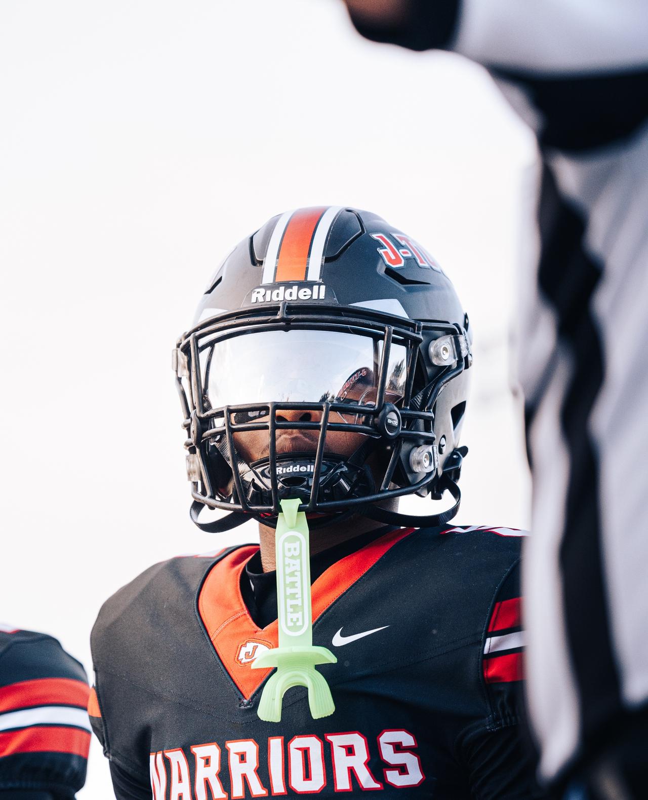 Warriors player in a black helmet with a glowing green mouthguard hanging from his facemask
